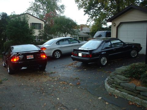 2002 Ford Mustang - Three cars are parked in a driveway next to a house and garage.