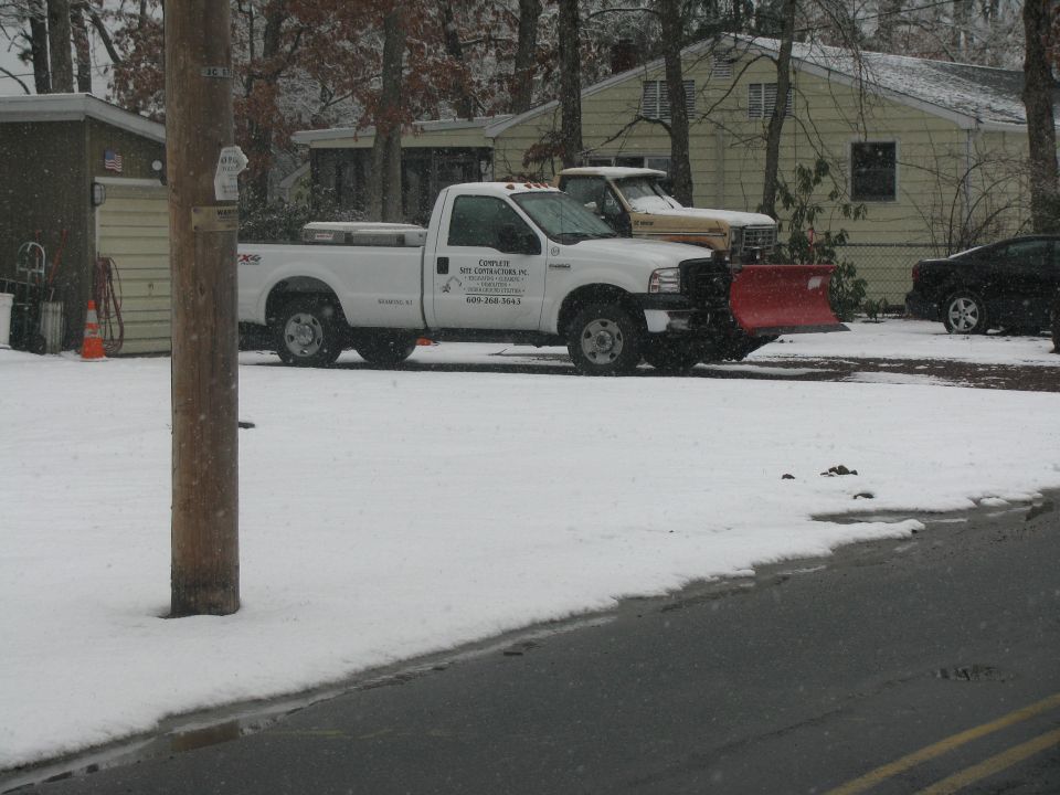 White pickup truck with a red snow plow, parked in snow. Text on door reads 'Cowles Site Contractors Inc.'
