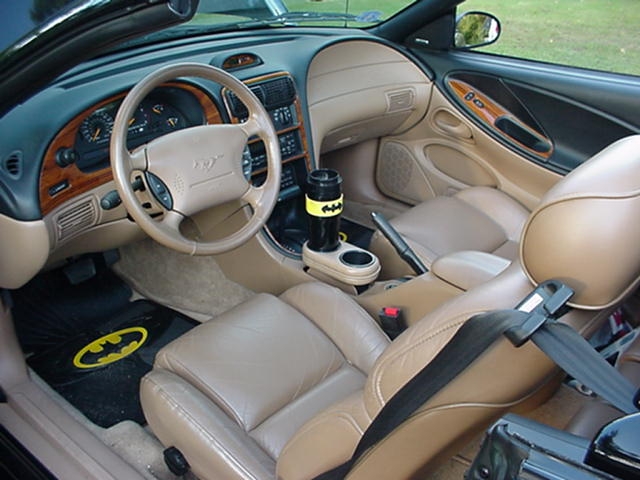 1996 Ford Mustang interior with tan leather seats, wood trim, and Batman floor mats