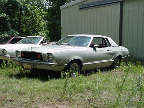 1976 Ford Mustang II - Two cars parked in front of a building, one is a 1976 Ford Mustang II coupe.