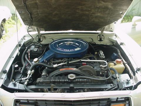 1976 Ford Mustang II - The engine bay of a 1976 Ford Mustang II is shown with the hood raised, revealing the V8 engine and its components.