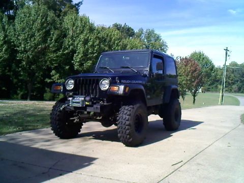 1995 Ford Bronco - A modified Jeep Wrangler sits parked on a driveway with trees in the background.