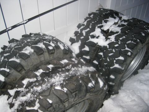 1990 Ford Bronco - Off-road tires are piled up and covered in snow.