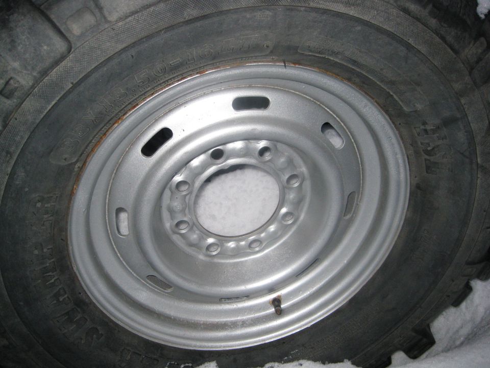 Close-up of a silver steel wheel with a knobby tire. Snow is visible around the wheel