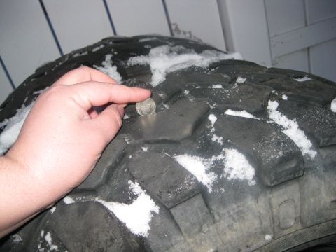 1990 Ford Bronco - A hand holds a coin against the deep tread of a tire covered in snow, suggesting a measurement of tread depth.