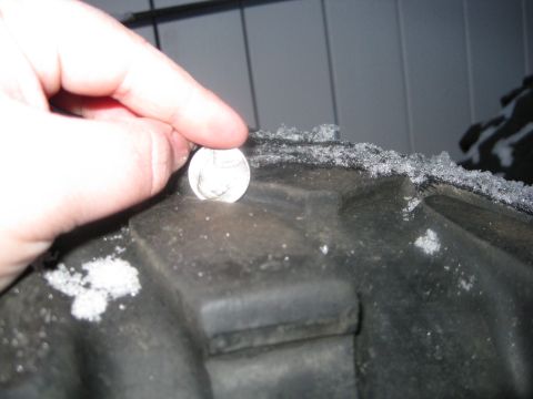 1990 Ford Bronco - A coin is placed on a tire tread to show its depth, with snow visible on the tire.