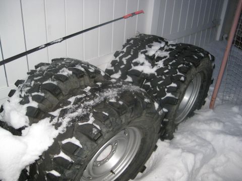 1990 Ford Bronco - Several large off-road tires are piled up in the snow, suggesting preparation for winter conditions.