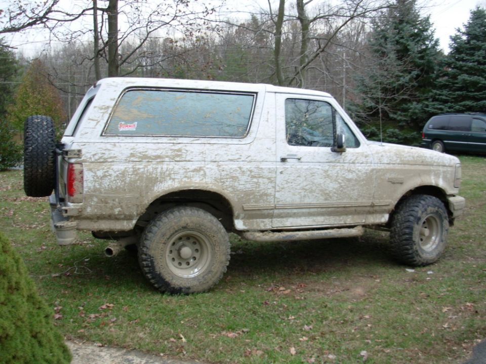 Mud-covered white 1990s Ford Bronco SUV, side view, lifted on off-road tires