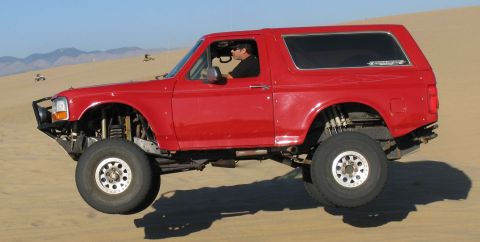 1984 Ford Bronco - A red Ford Bronco navigates sand dunes with its front wheels airborne.