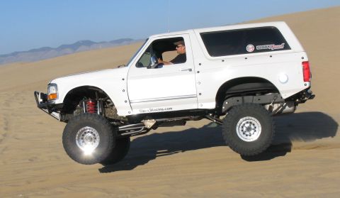 1984 Ford Bronco - This heavily modified Ford Bronco is captured mid-air while navigating a sandy terrain, its off-road capabilities.