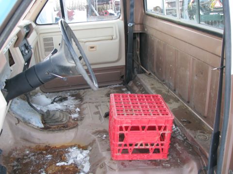 1982 Ford F-150 - The interior of a truck cab shows a worn dashboard, steering wheel, and floor with snow and rust.