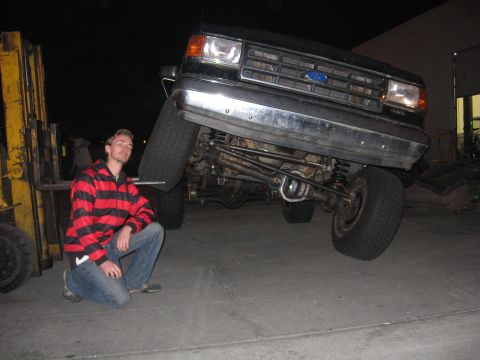 1989 Ford Bronco - Man kneels next to a 1989 Ford Bronco being lifted by a forklift.