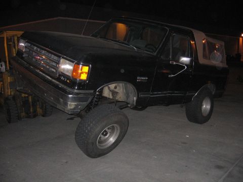 1989 Ford Bronco - A black Ford Bronco with a tan soft top is being lifted by a forklift.