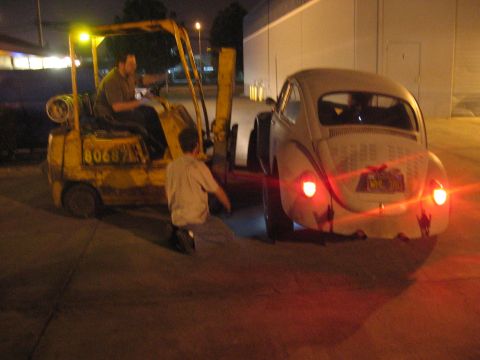 1989 Ford Bronco - A forklift is used to move a classic Volkswagen Beetle in a dimly lit outdoor area at night.