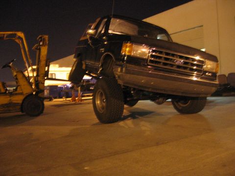 1989 Ford Bronco - A black 1989 Ford Bronco is lifted by a forklift, showing its front 3/4 view.