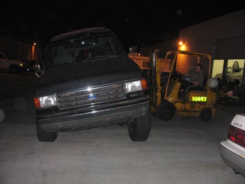 1989 Ford Bronco - A black 1989 Ford Bronco is parked next to a yellow forklift at night.