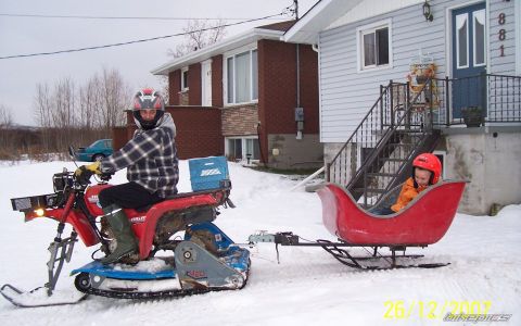 2000 Ford E350 - A person rides a red snowmobile that is towing a red sleigh with a child in it through the snow.