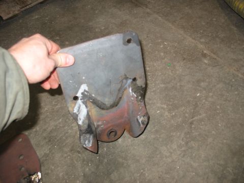 1995 Ford C-350 (Centurion Conversions) - A metal bracket, likely a rear spring hanger, is held by a hand. It shows signs of welding and wear.