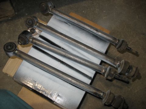 1995 Ford C-350 (Centurion Conversions) - Four metal suspension control arms with rubber bushings are laid out on a surface.