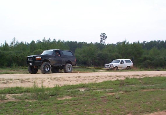 Black lifted Bronco being pulled by a white Bronco on sandy ground