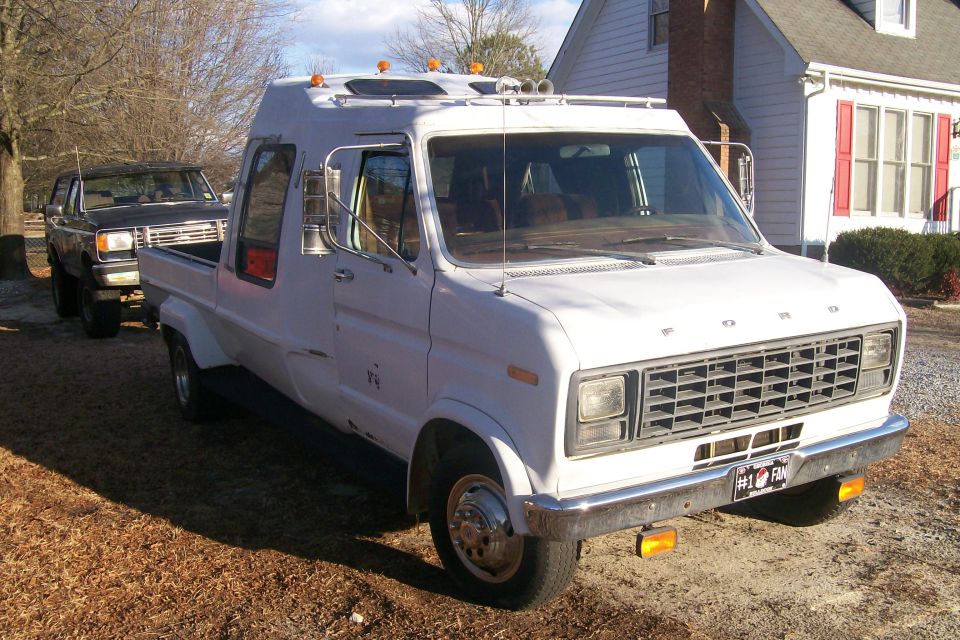 White Ford van converted to a pickup, 3/4 front view parked beside a house