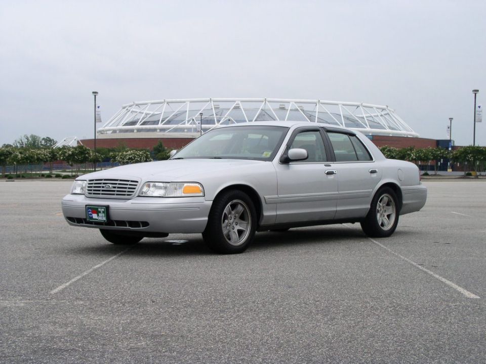 Silver 2001 Ford Crown Victoria parked in a lot with a stadium in the background