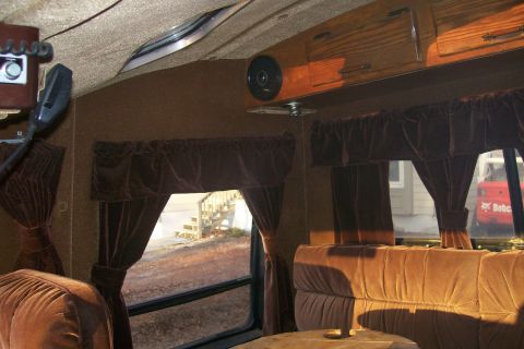 1982 Ford E350 - The interior of a van shows brown velour seating and curtains, with a Bobcat vehicle visible outside.