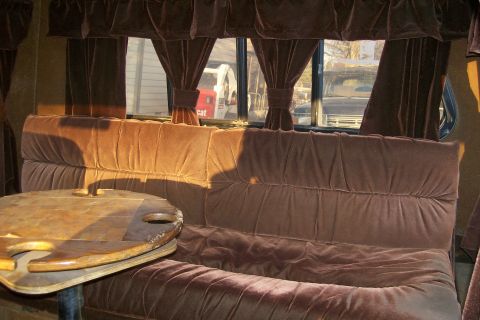 1982 Ford E350 - The interior of a van features plush brown velvet seating and a fold-out table, with glimpses of construction equipment and another vehicle…