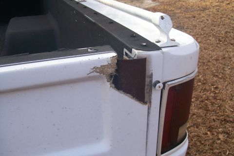1982 Ford E350 - Close-up of the damaged rear corner of a white pickup truck bed, revealing exposed material beneath the paint.