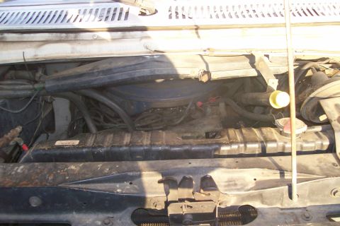 1982 Ford E350 - The engine bay of a white van shows a radiator and various hoses and engine parts.