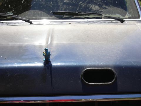 1991 Ford Bronco - A blue toy figure is mounted on the hood of a dusty blue vehicle. An oval-shaped air intake with a ribbed black surround is visible on the…