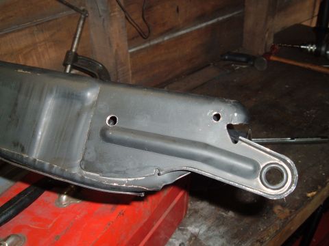 1990 Ford Ranger - A close-up view of a dark gray, possibly metal, automotive part with two circular holes and a rubber bushing. The part is clamped to a wood…