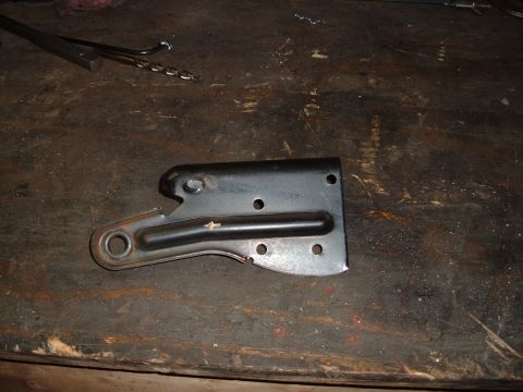1990 Ford Ranger - A black metal bracket with several holes and a circular opening is shown on a dark, worn wooden surface. Tools, including a drill bit, are…