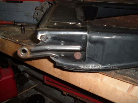 1990 Ford Ranger - A close-up view shows a black metal automotive part with a silver bracket attached via bolts, resting on a wooden workbench. Tools and a re…