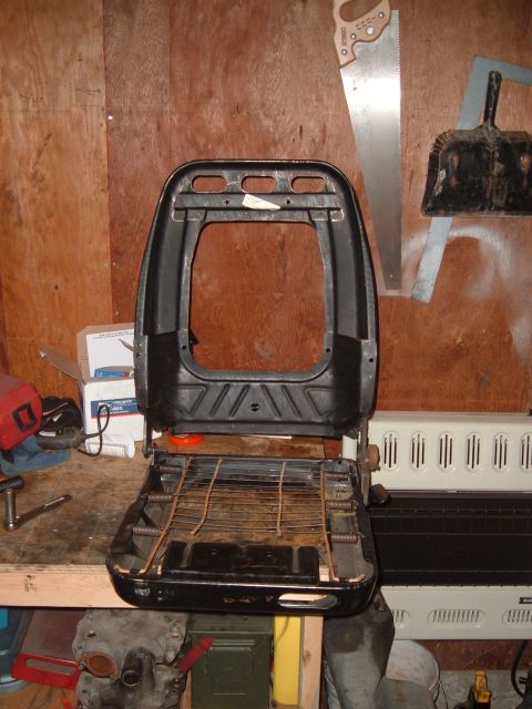 1990 Ford Ranger - A disassembled black car seat base with a metal spring support system is shown in a workshop setting. Tools and other items are visible on…