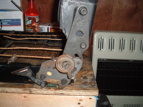 1990 Ford Ranger - A close-up view of a metal seat adjustment mechanism with springs and bolts, attached to a black seat frame with wooden slats. A bottle of…