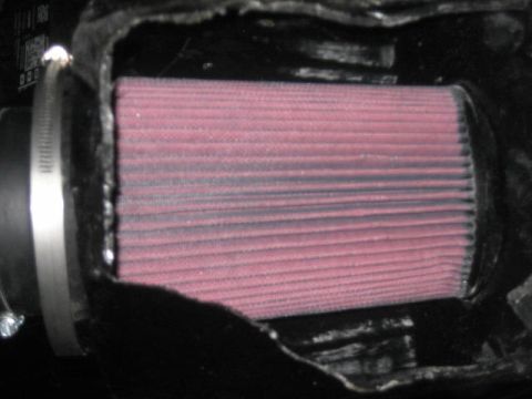 1996 Ford Thunderbird - A close-up view of a red, pleated air filter secured within a black housing by a metal clamp.