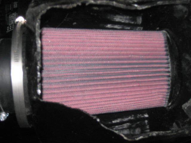 Red pleated air filter in black housing with metal clamp
