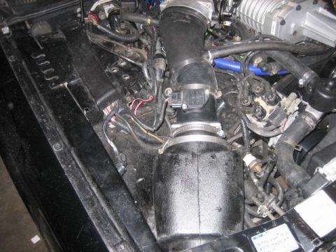 1996 Ford Thunderbird - A close-up view of a modified engine bay, featuring a black air intake system with a silver supercharger visible at the top right. Various…