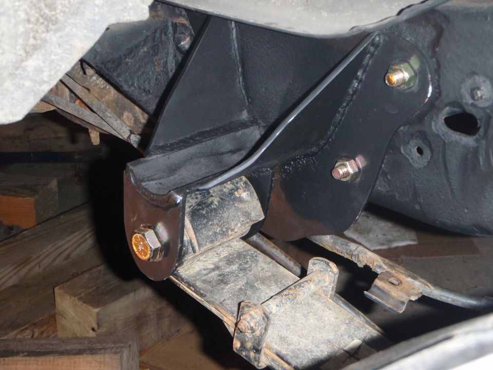Aftermarket black bracket attached to vehicle frame and leaf spring.