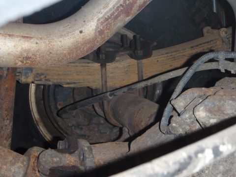 1996 Ford Bronco - This image shows the underside of a vehicle, focusing on the rear axle assembly with leaf springs, U-bolts, and brake components. A portion…
