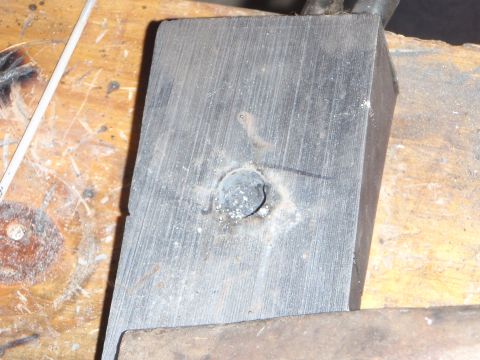 1996 Ford Bronco - A close-up shot shows a metal block with a hole drilled in it, resting on a wooden surface. The block appears to be part of a mechanical pr…