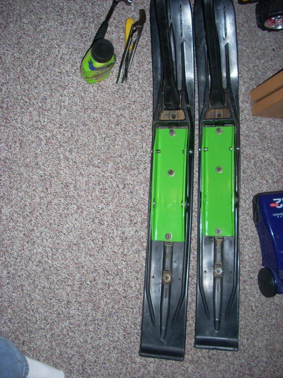 Pair of skis with bindings on carpet next to tools and a bottle.