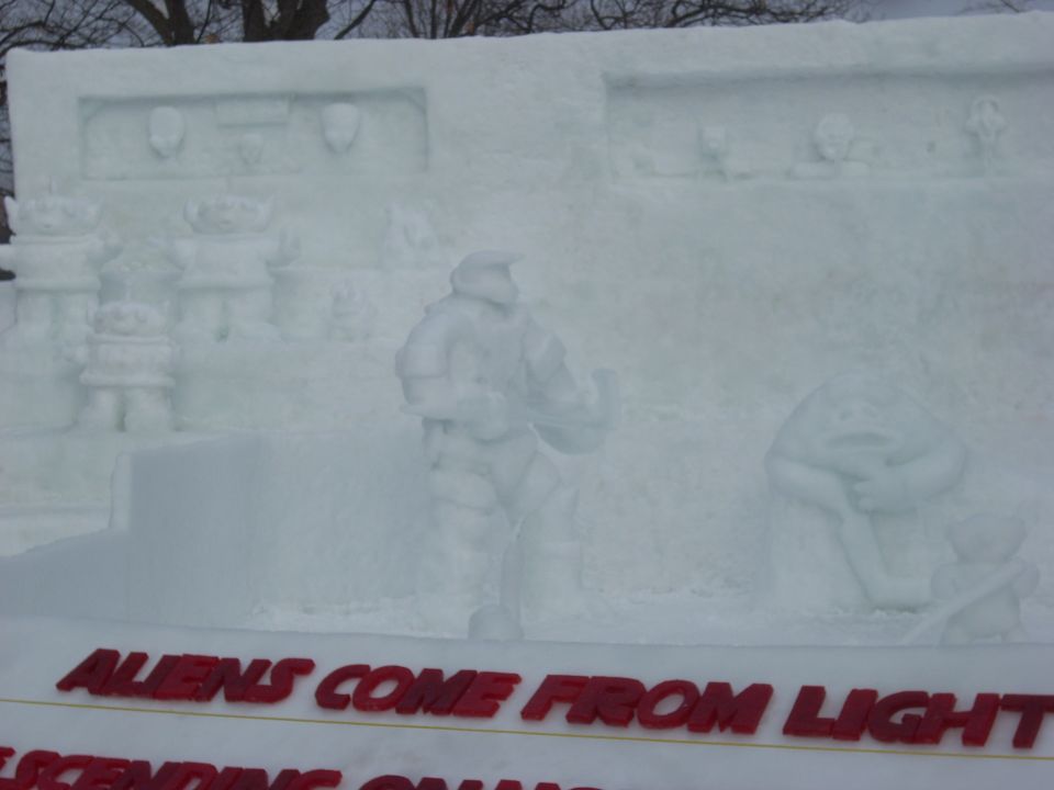 Snow sculpture with aliens and a space marine figure, text reads "ALIENS COME FROM LIGHT"
