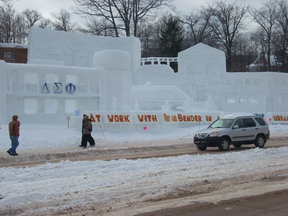 Silver SUV in front of a snow sculpture with a banner.