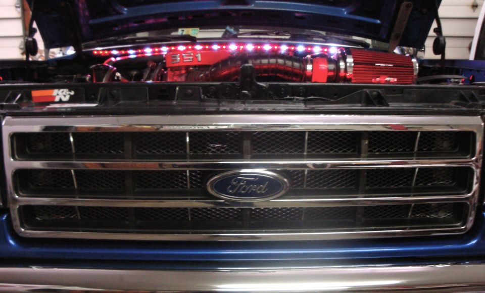 Front chrome Ford grille under open hood revealing red 351 engine with LED light strip and K&N sticker