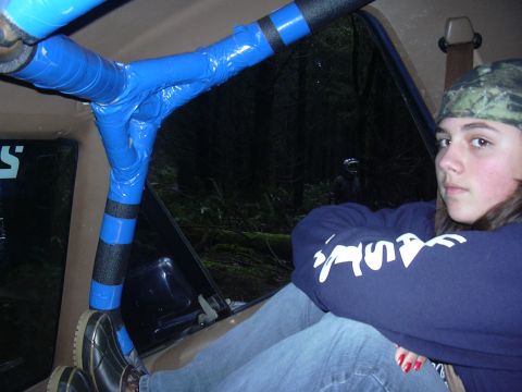1991 Ford Bronco - Interior view of a vehicle with a roll cage wrapped in blue tape and black foam padding. A person wearing a camouflage hat and a blue sweat…