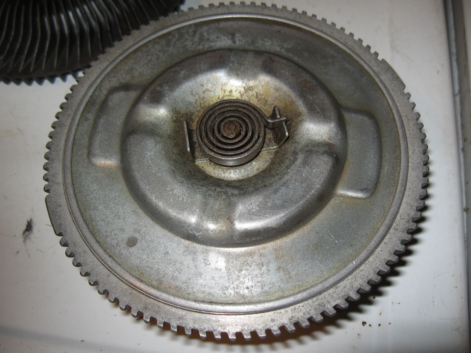 Metal flywheel with toothed edge and central coiled spring mechanism.