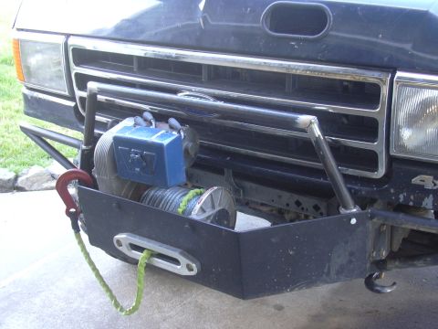 1991 Ford Bronco - Close-up of a dark blue Ford truck's front end fitted with a black fabricated winch bumper housing a blue-bodied winch with synthetic line,…