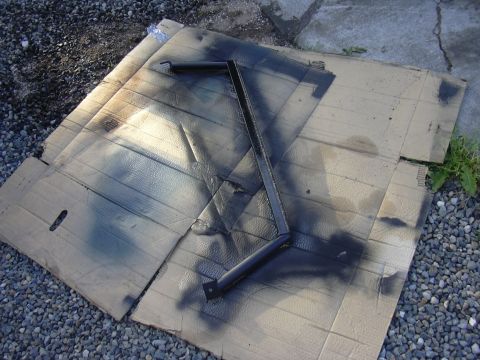 1991 Ford Bronco - A metal bracket is spray painted black and placed on cardboard.